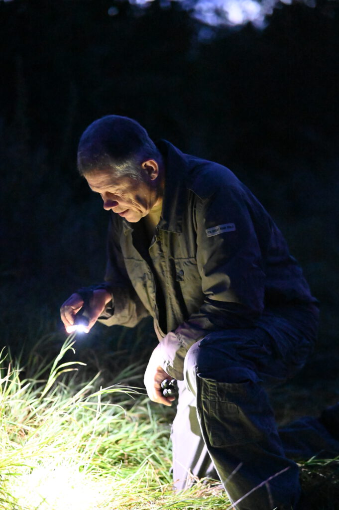 In der Nacht ist Oliver Solbach im Wald. In unauffälliger Kleidung untersucht er mit seiner Taschenlampe etwas im Gras.