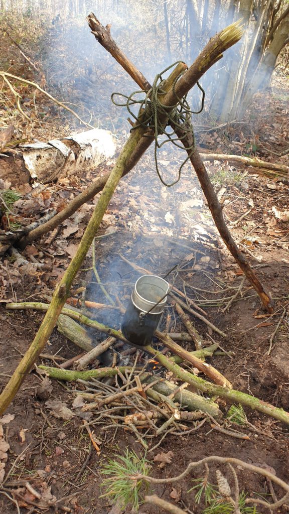 Feuerstelle mit Gestell für Kochgeschirr beim Lagerbau. Hier Dreibein zusammengebunden.